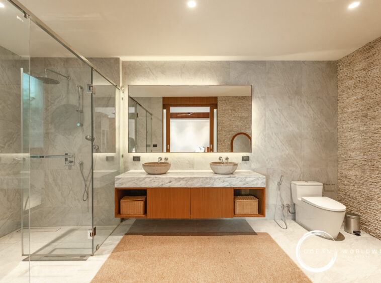 Modern bathroom with glass shower enclosure, double marble sinks, and a large framed mirror above a wooden vanity.