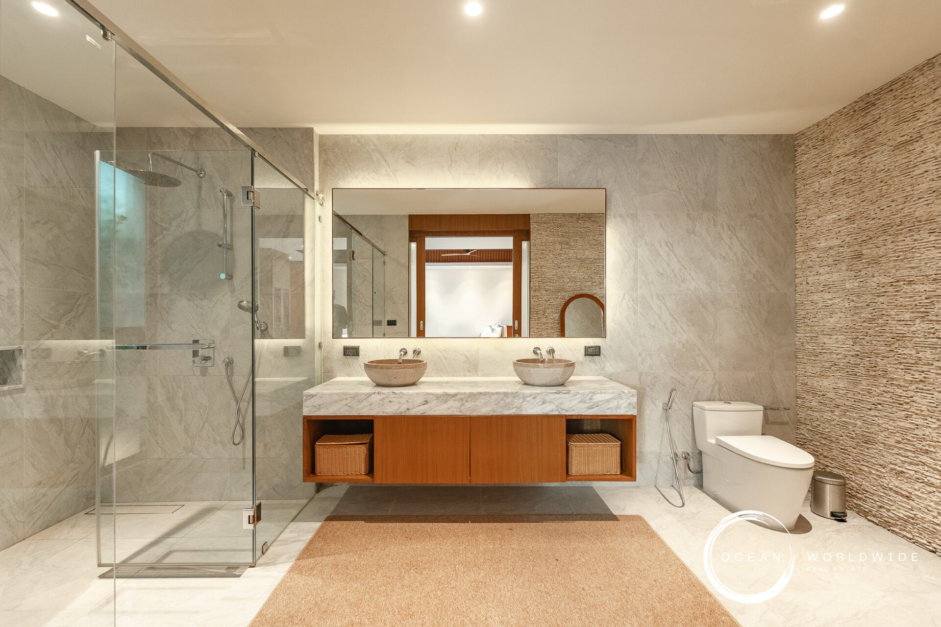 Modern bathroom with glass shower enclosure, double marble sinks, and a large framed mirror above a wooden vanity.