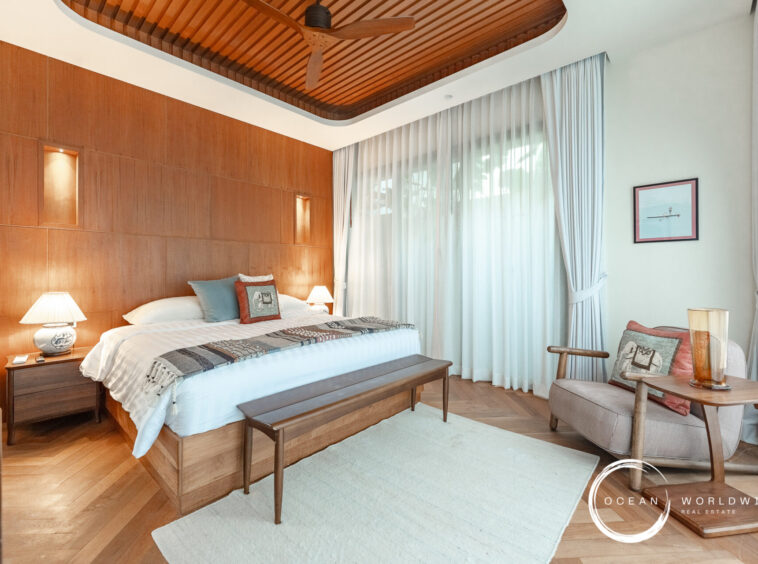 Hotel bedroom with a king bed, wood-paneled headboard, and two bedside lamps. A bench sits at the foot of the bed.