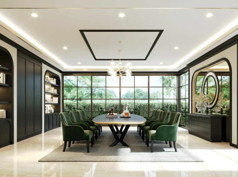 Luxurious dining room with a long oval table, green upholstered chairs, black cabinetry, and large windows letting in daylight.