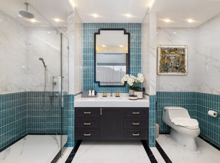 Luxurious bathroom with teal tile accents, a black double-drawer vanity, and a mirror above a marble countertop with white flowers and accessories.
