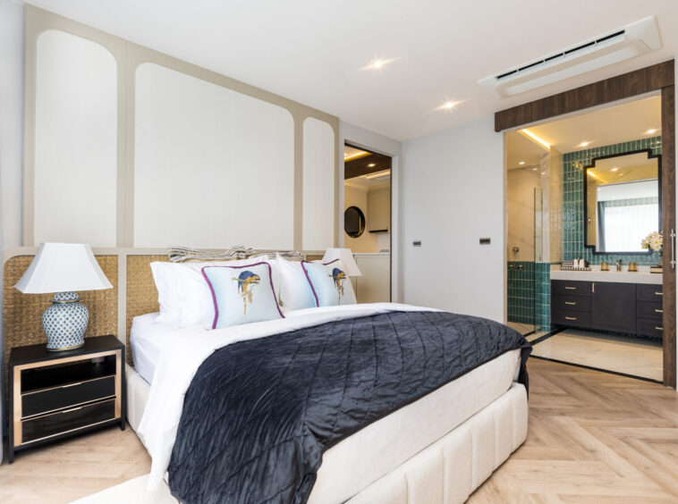 Luxurious hotel bedroom with a king bed, tufted headboard, and an ensuite bathroom nearby with green-tiled walls.