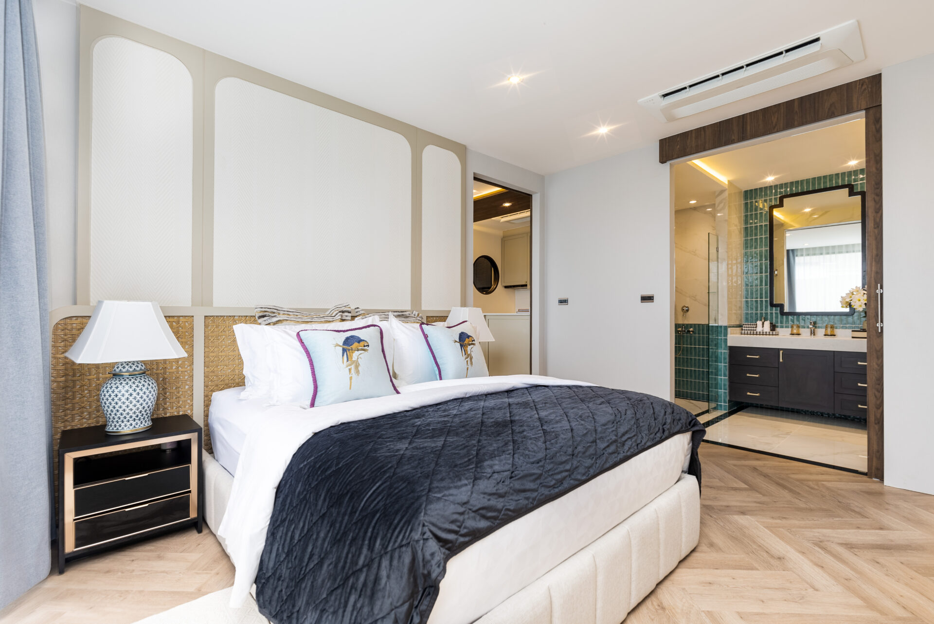 Luxurious hotel bedroom with a king bed, tufted headboard, and an ensuite bathroom nearby with green-tiled walls.