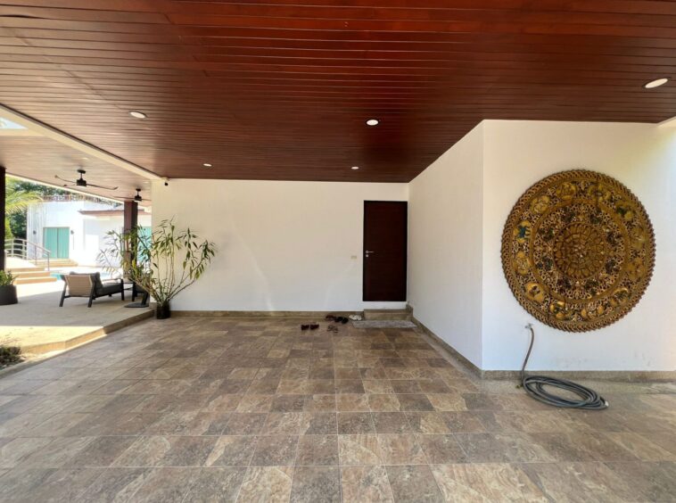Covered outdoor patio with a wood-paneled ceiling, white walls, and a large ornate gold circular wall art (mandala).