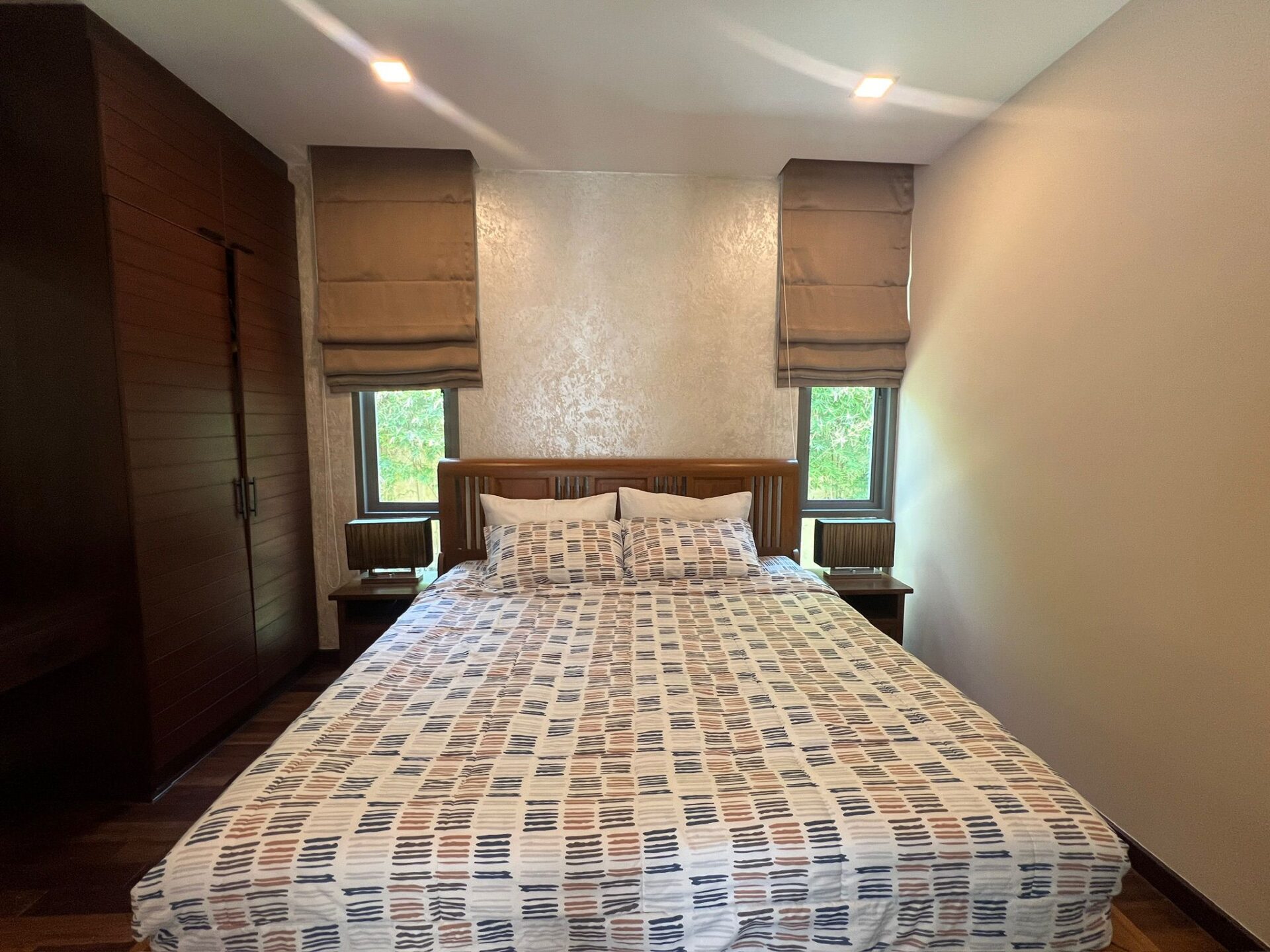 A neatly made double bed with a patterned duvet flanked by two dark wooden nightstands in a modern bedroom.