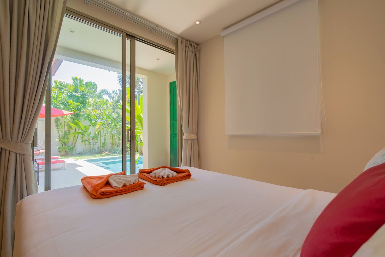 Hotel bedroom with a sliding glass door to a pool deck, white bedding, and orange folded towels on the bed.
