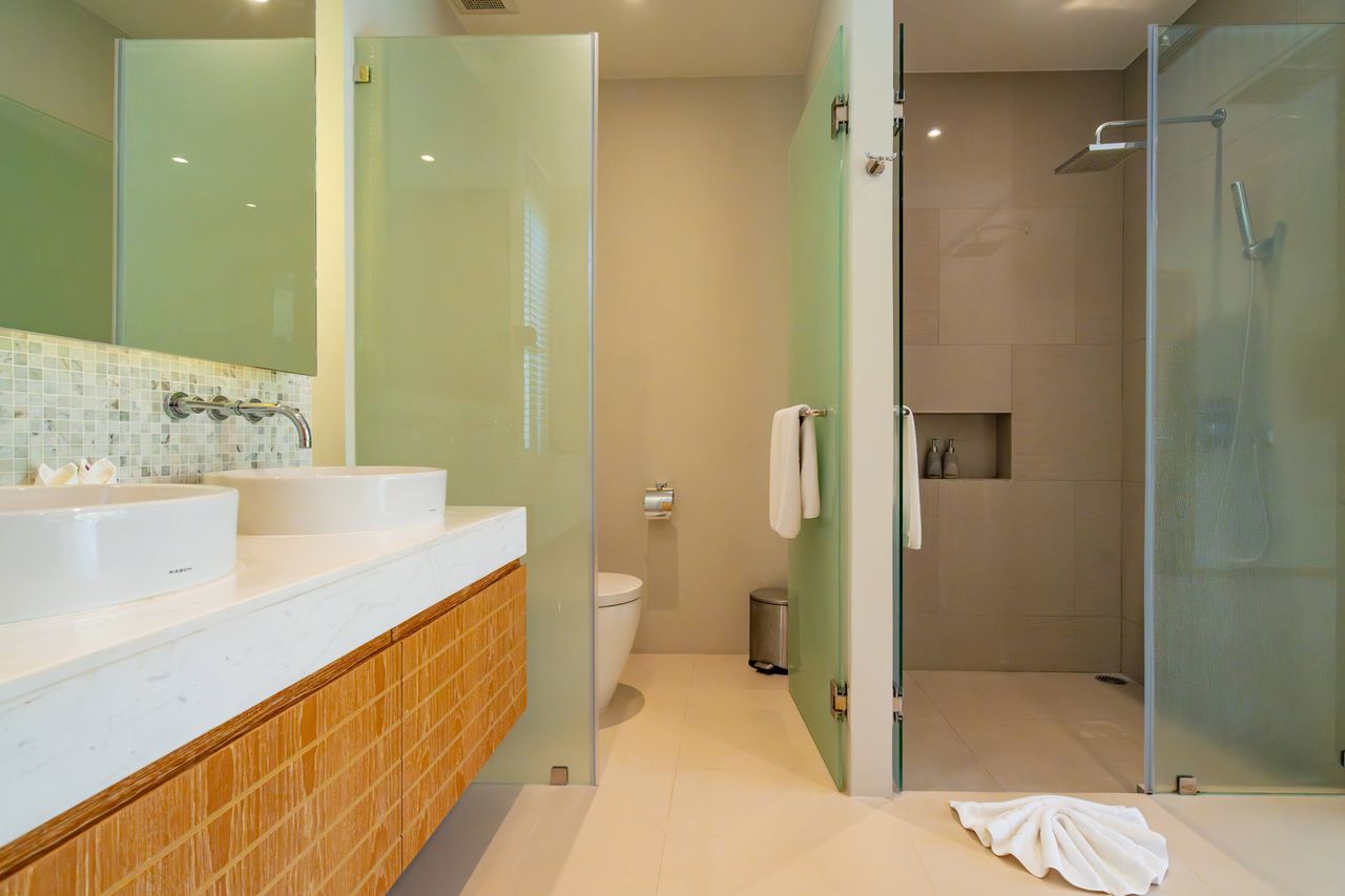 Modern bathroom with a double vanity, two round vessel sinks, and a glass-enclosed shower area.