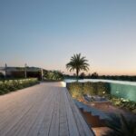 Sunset view over a luxurious rooftop pool area with palm trees, a wooden deck, and lounge chairs.