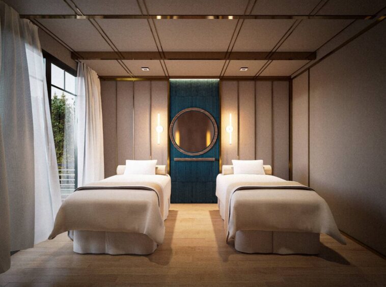 Twin hotel room with two single beds, beige bedding, and a blue paneled wall featuring a round mirror between warm wall lamps on either side.