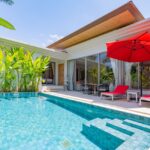 Modern backyard with a turquoise pool, red sun loungers, and a large red patio umbrella beside glass doors.