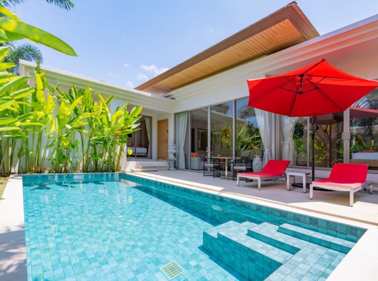 Modern backyard with a turquoise pool, red sun loungers, and a large red patio umbrella beside glass doors.