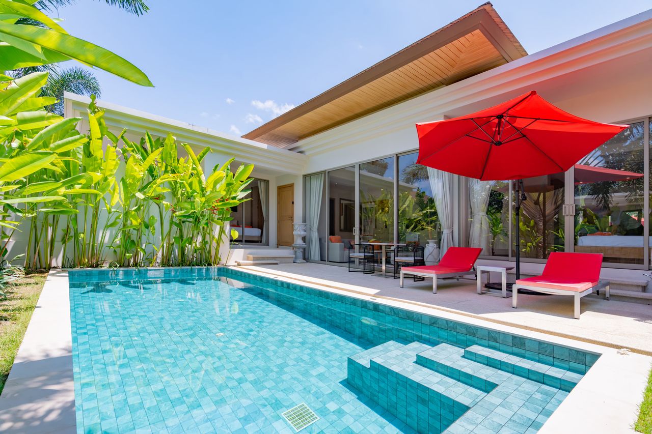 Modern backyard with a turquoise pool, red sun loungers, and a large red patio umbrella beside glass doors.