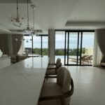 Open-plan kitchen and dining area with a white marble island, wicker chairs, and large glass doors opening to a pool and outdoor seating.