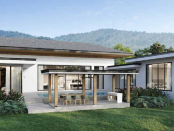 Modern single-story house with flat roof, large glass walls, and a covered poolside dining area in a landscaped yard with mountains in the background.