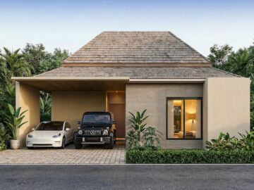Modern single-story house with a wooden shingle roof; driveway under a carport holds a white sedan and a black SUV, surrounded by tropical plants.