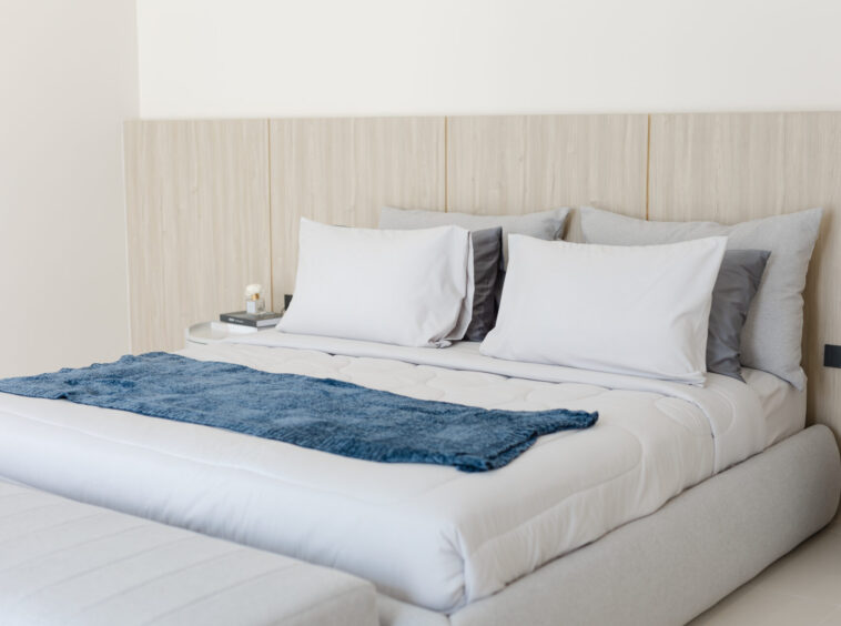Hotel-style bedroom with a large bed, white linens, gray and white pillows, and a blue throw across the foot of the bed.