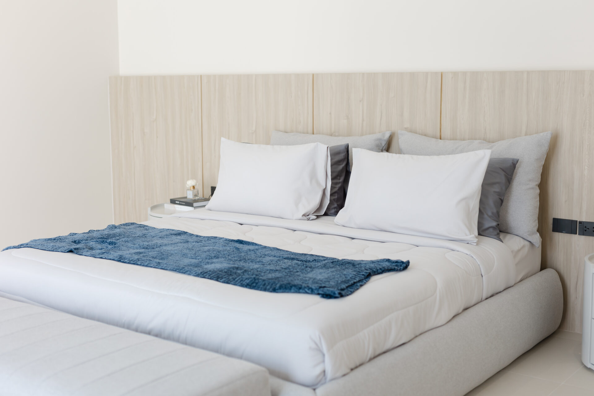 Hotel-style bedroom with a large bed, white linens, gray and white pillows, and a blue throw across the foot of the bed.