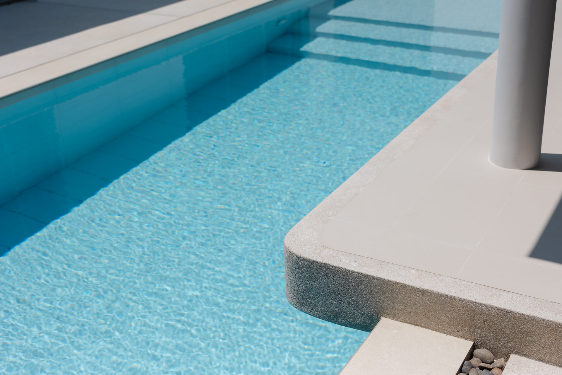 Pool edge beside a clear blue pool with stepped entry and a light gray tiled deck.