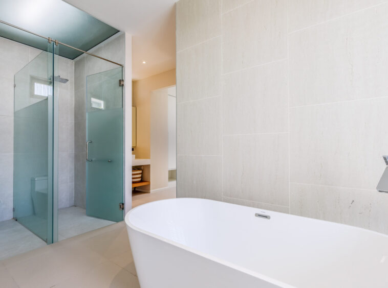Modern bathroom with a glass-walled shower, frosted doors, and a white freestanding tub in a neutral-toned space.