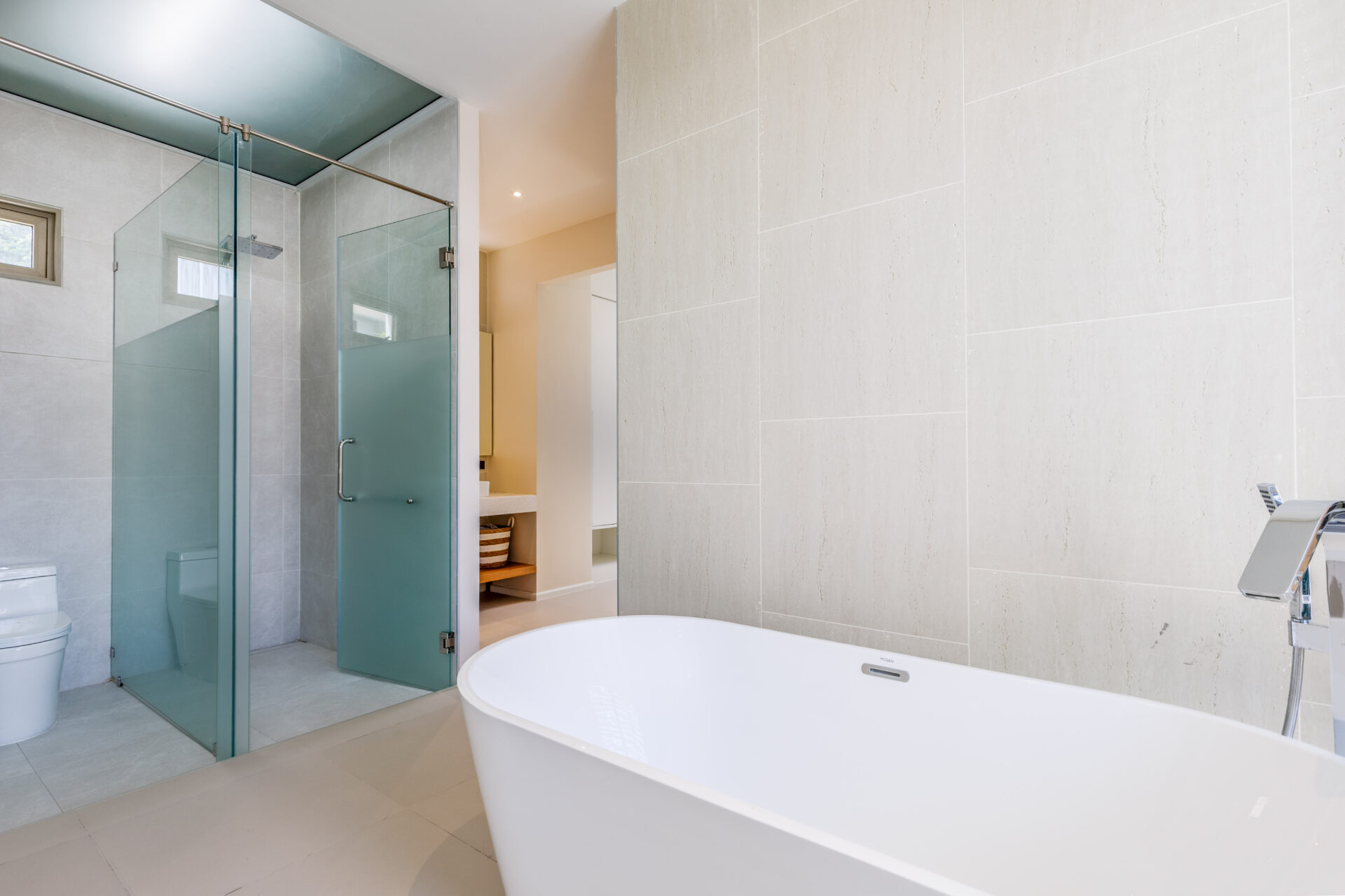 Modern bathroom with a glass-walled shower, frosted doors, and a white freestanding tub in a neutral-toned space.