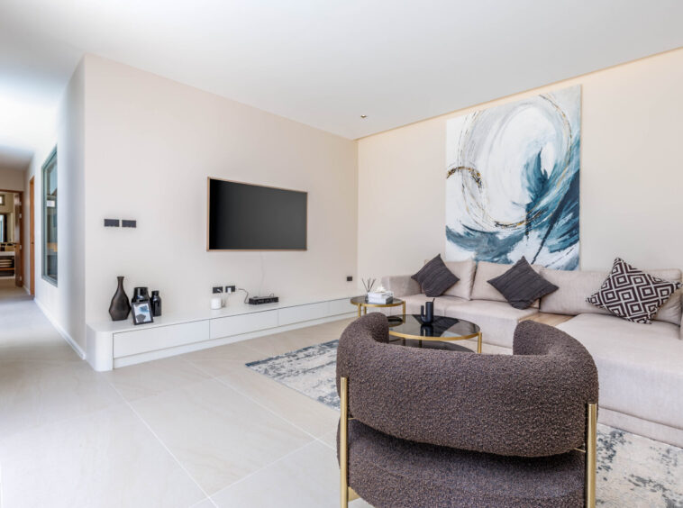 Living room with beige sectional, two dark throw pillows, glass coffee table, and a large abstract swirl painting on the wall.