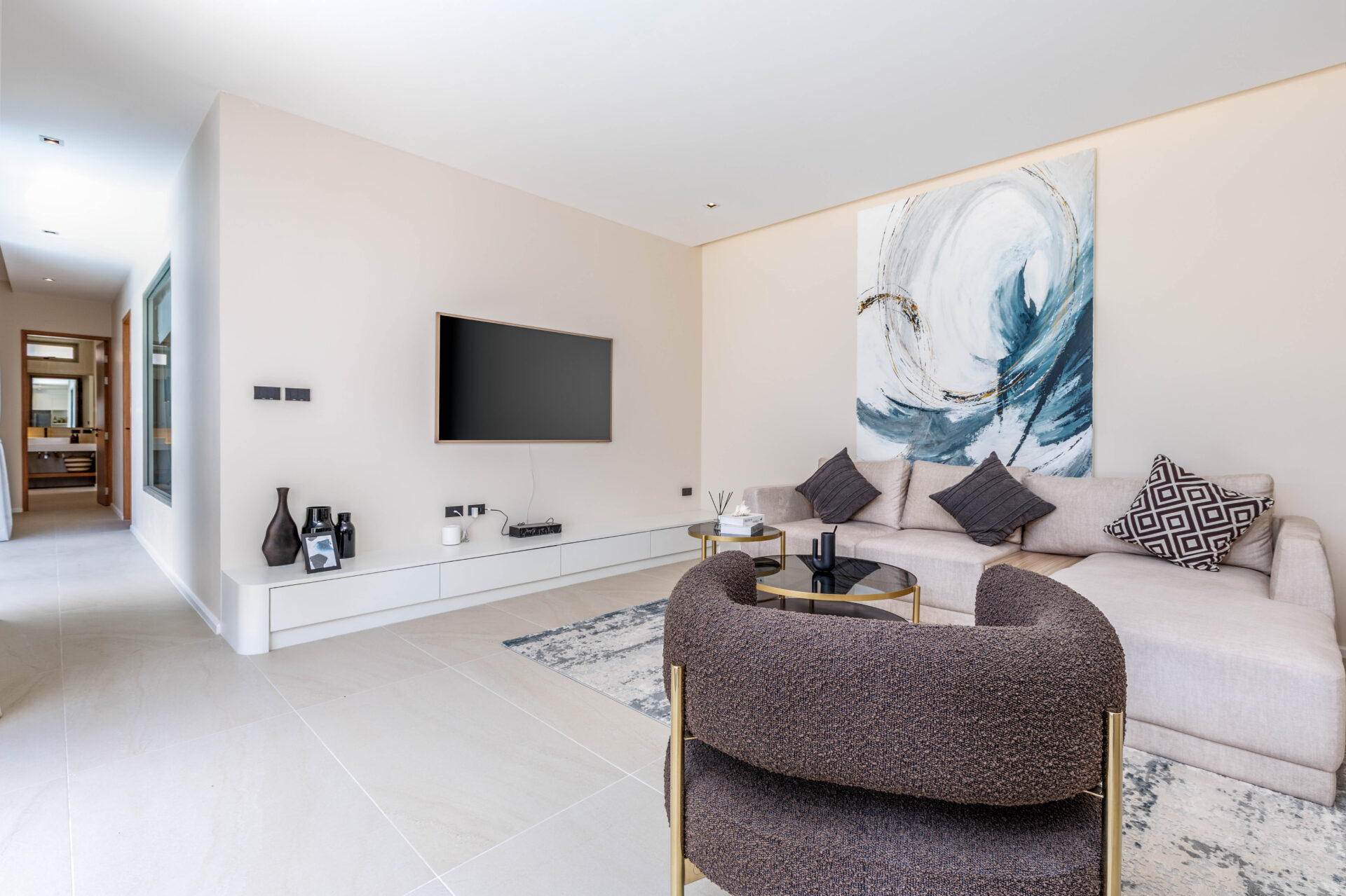 Living room with beige sectional, two dark throw pillows, glass coffee table, and a large abstract swirl painting on the wall.