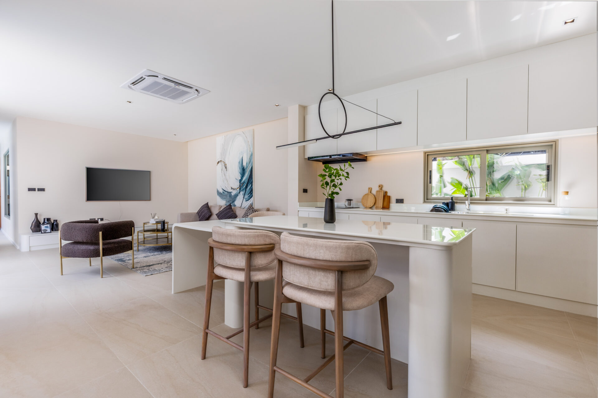 Open-plan kitchen and living area with white cabinets, a marble light-toned island, beige bar stools, and a wall-mounted TV in the living room.