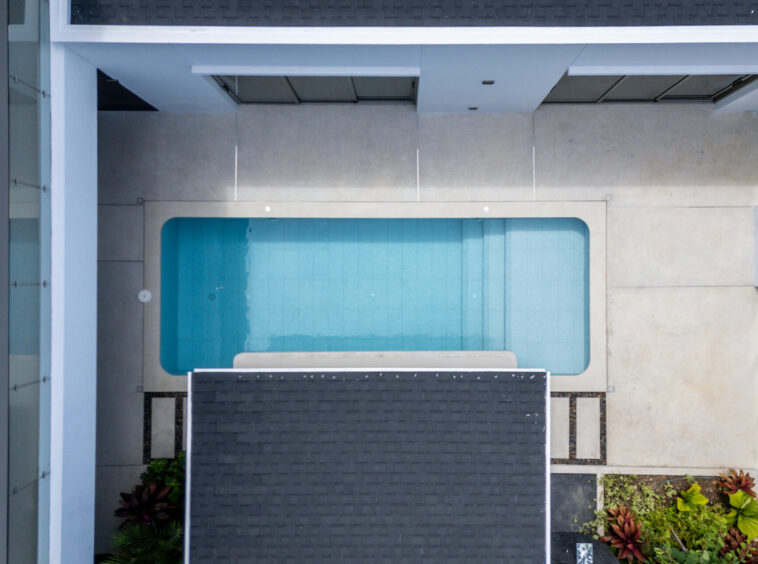 Aerial view of a rectangular rooftop pool surrounded by light-colored walls and dark shaded panels.