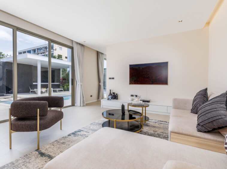 Bright living room with floor-to-ceiling glass doors opening to a pool area and outdoor seating, modern neutral decor.