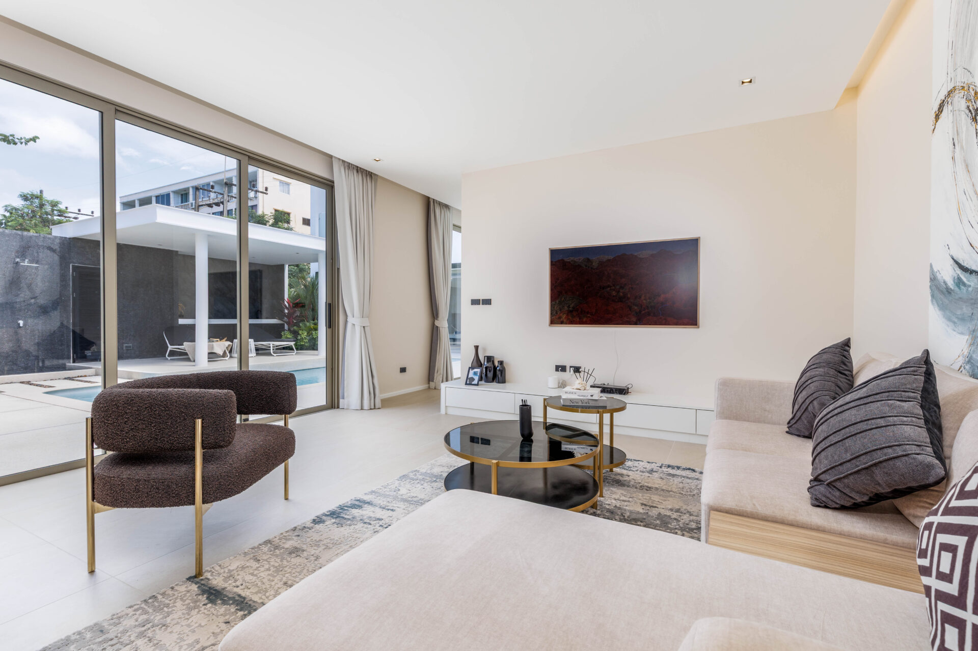 Bright living room with floor-to-ceiling glass doors opening to a pool area and outdoor seating, modern neutral decor.
