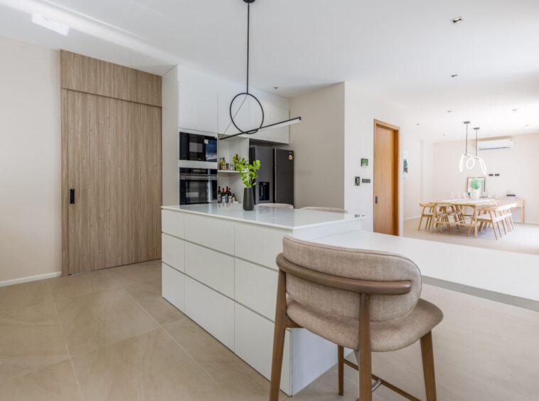 Open-plan kitchen with white cabinets, large island, and beige tiled floor; dining area visible in background.
