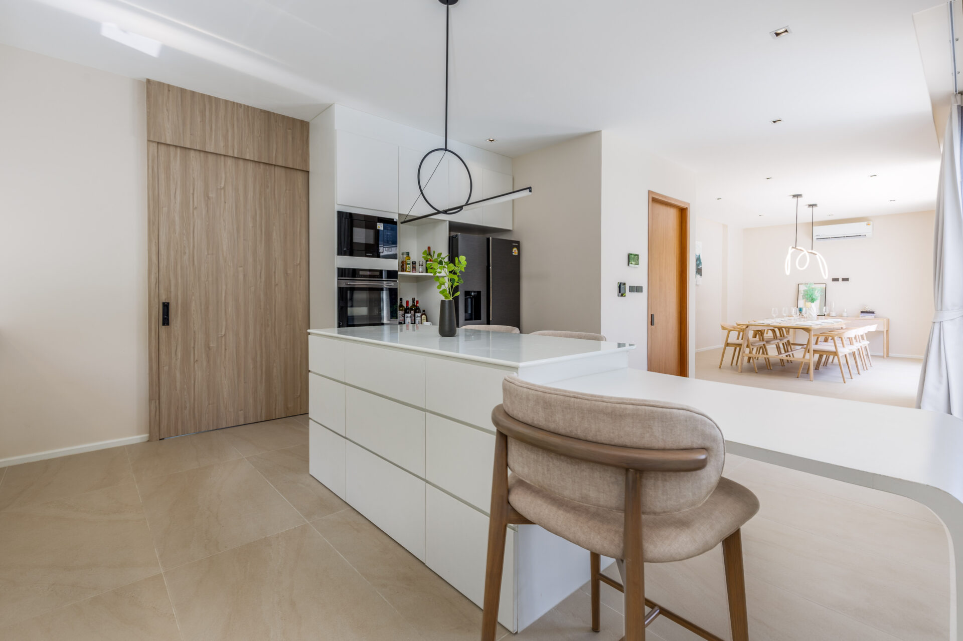 Open-plan kitchen with white cabinets, large island, and beige tiled floor; dining area visible in background.