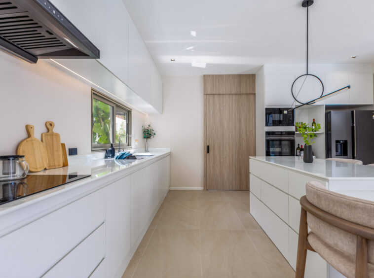 Bright modern kitchen with white cabinets, a long island, and stainless steel appliances; a circular pendant light and wooden door at the far end create a contemporary look.