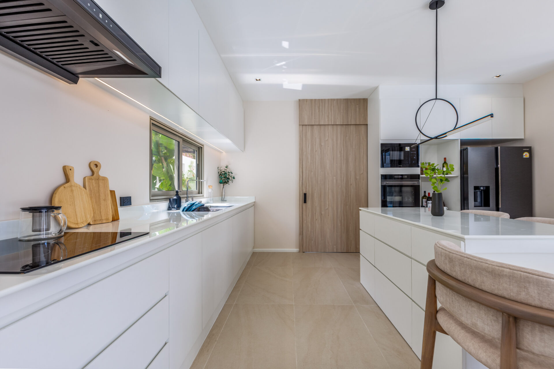 Bright modern kitchen with white cabinets, a long island, and stainless steel appliances; a circular pendant light and wooden door at the far end create a contemporary look.