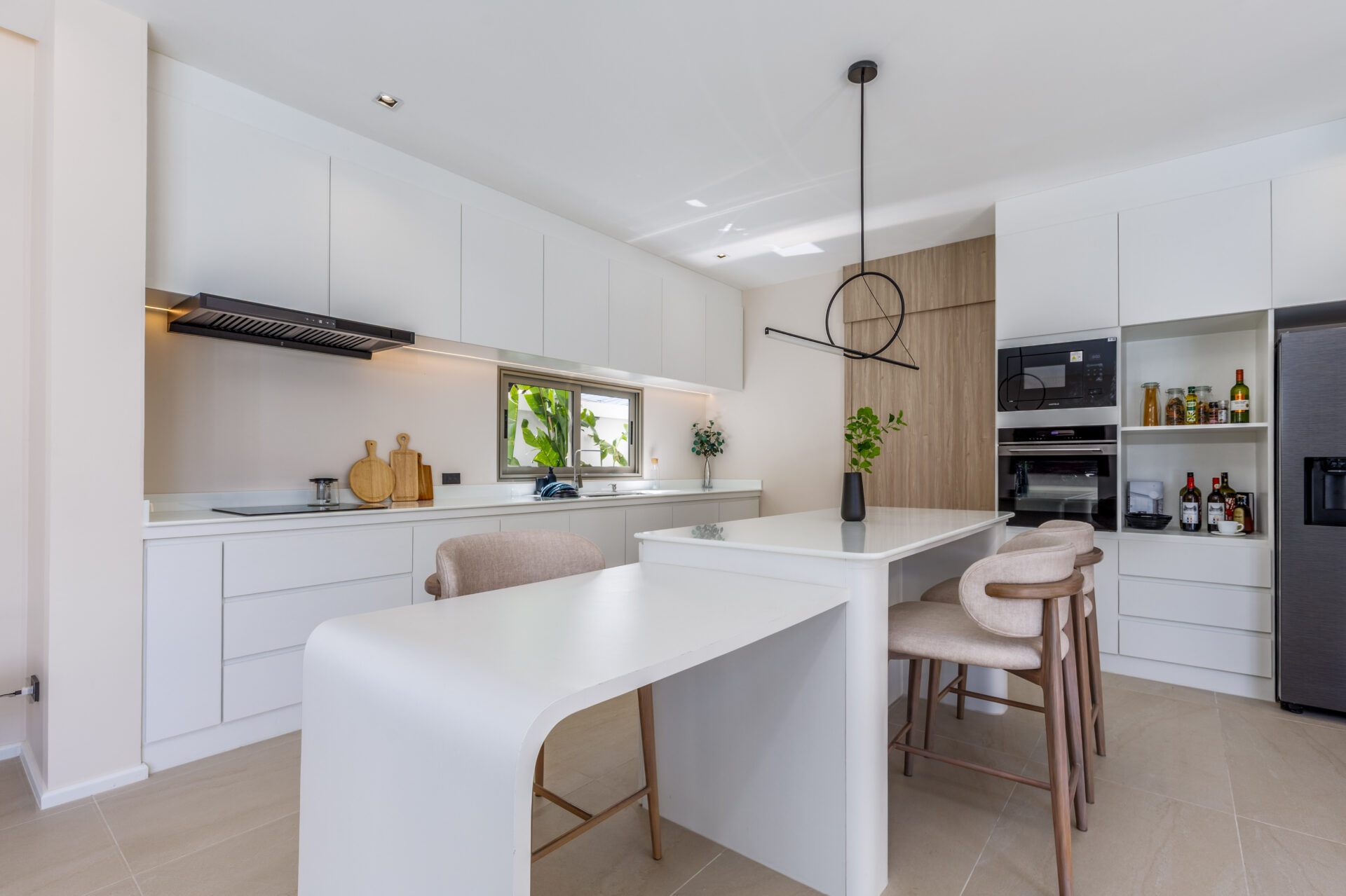 Bright white modern kitchen with a large island, beige bar stools, and a wall of cabinets and built-in oven.
