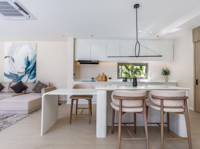 Open-plan kitchen and living area with white cabinets, an island, and beige seating beneath a large abstract painting on the left.