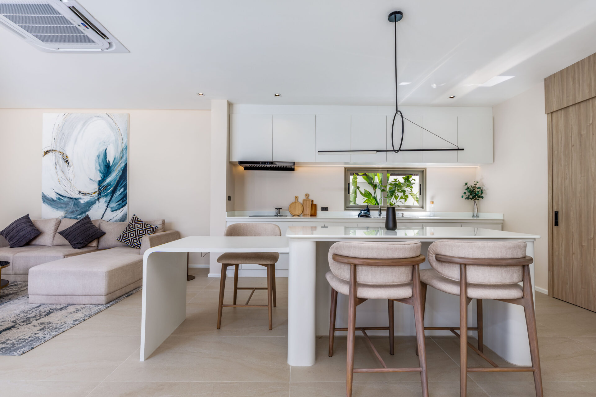 Open-plan kitchen and living area with white cabinets, an island, and beige seating beneath a large abstract painting on the left.