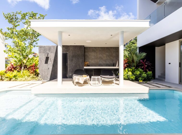 Modern backyard patio with a pool, white canopy, and lounge chairs under a shaded area.