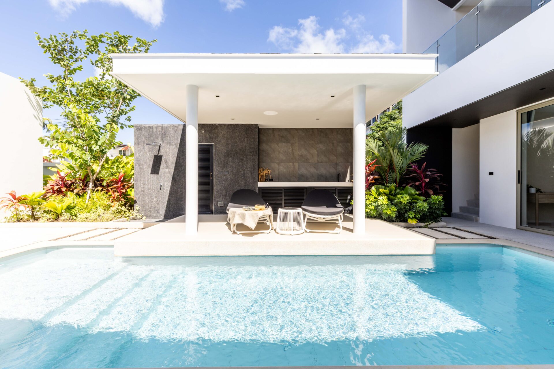 Modern backyard patio with a pool, white canopy, and lounge chairs under a shaded area.