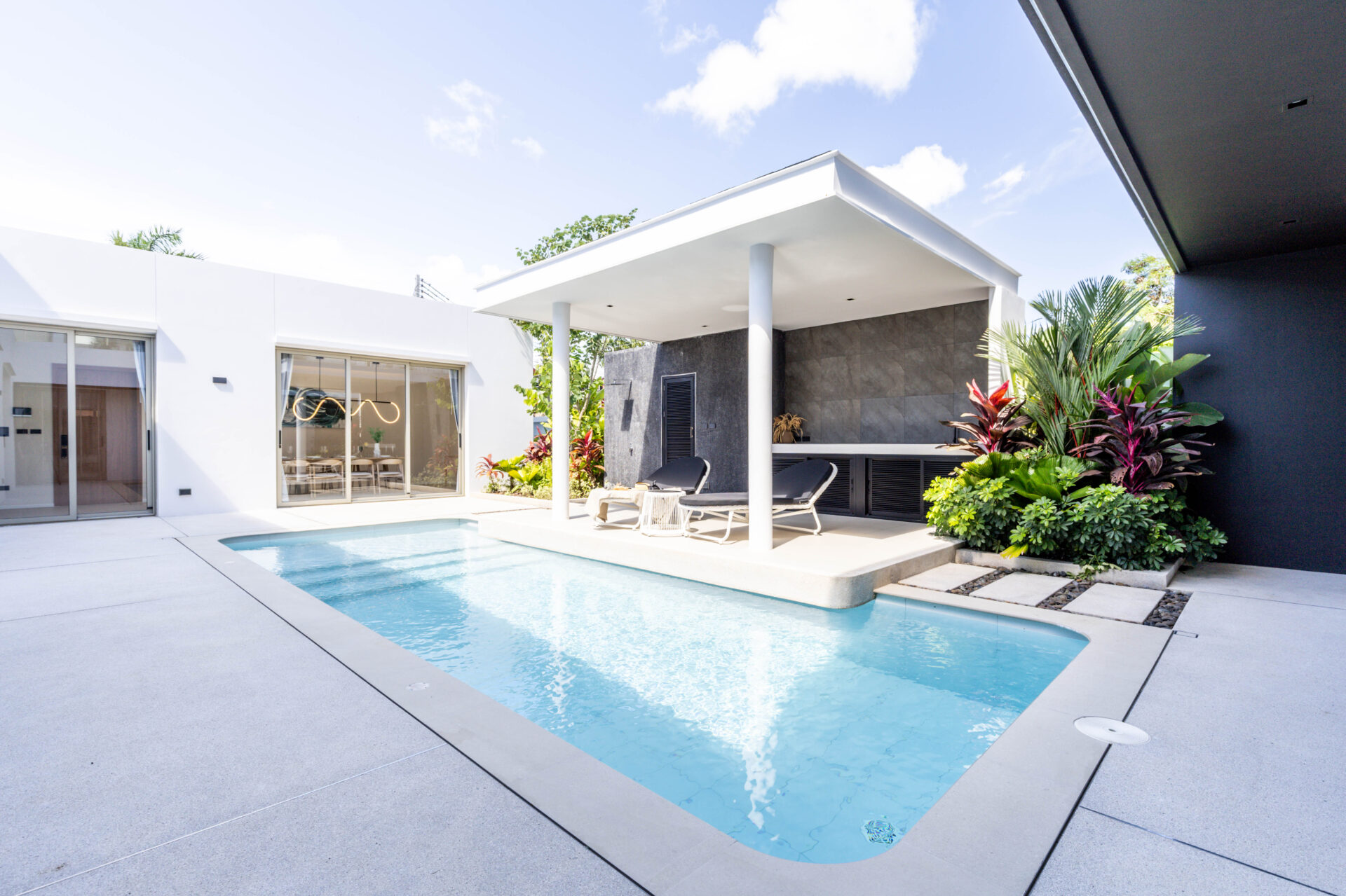 Modern backyard pool area with white patio, lounge chairs, and a shaded outdoor seating/kitchen zone under a white canopy.