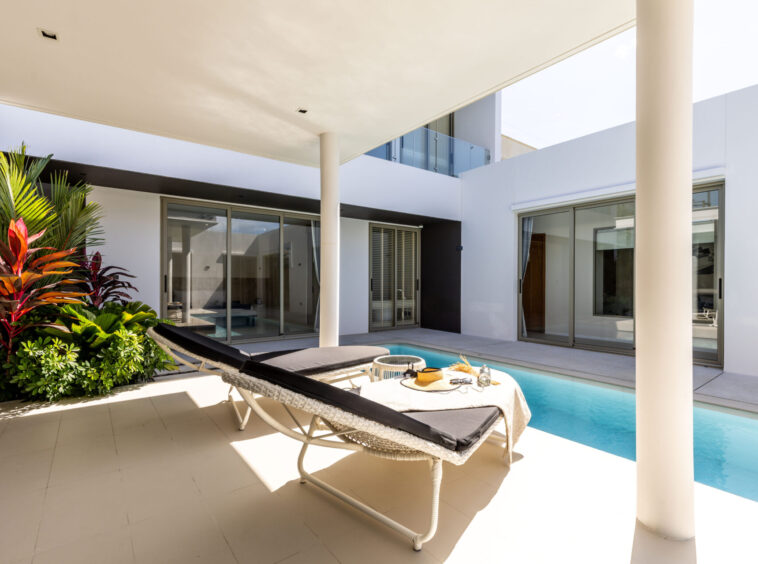 Modern backyard with a rectangular pool, two lounge chairs, and glass doors to the house interior.