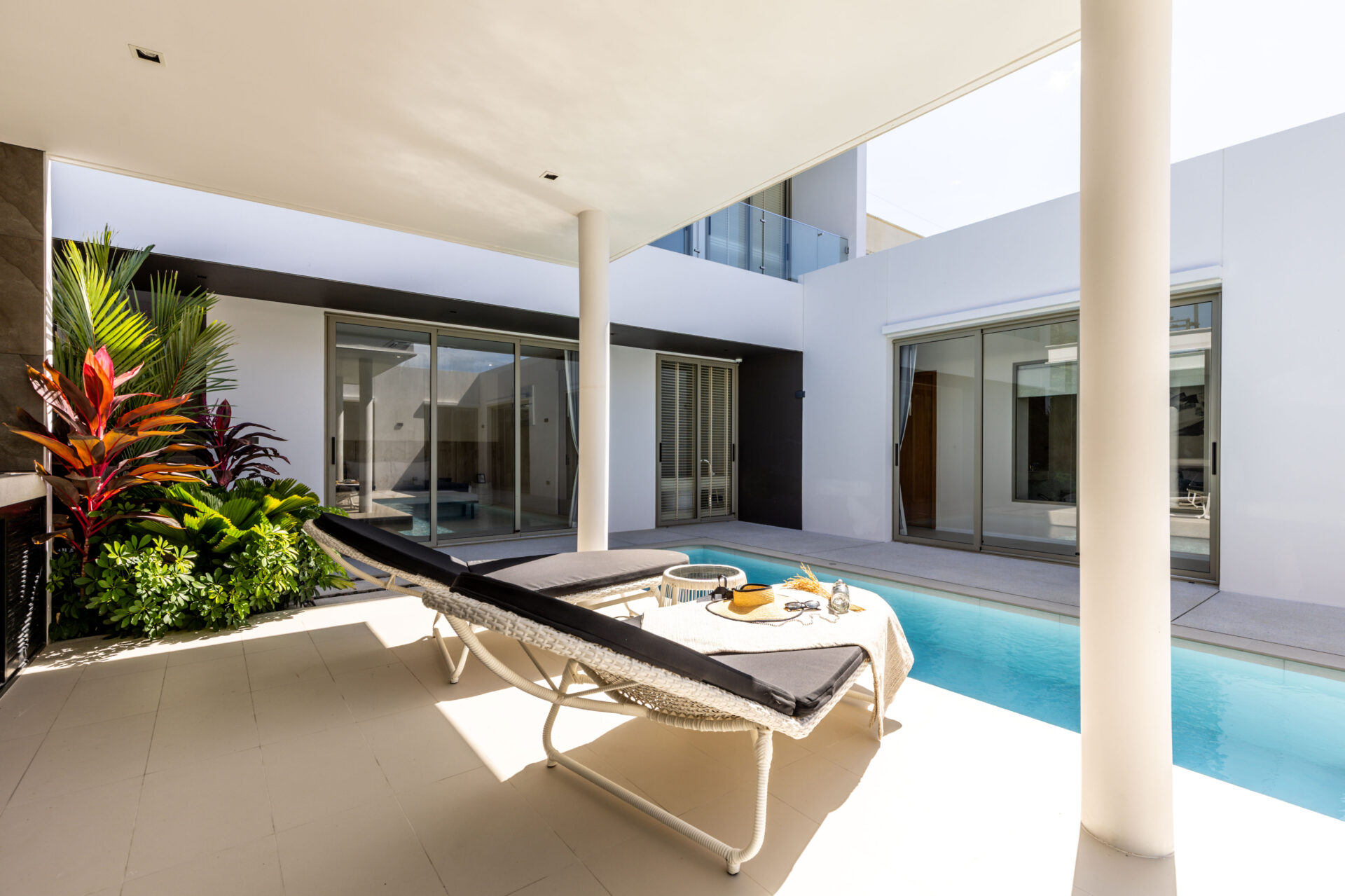 Modern backyard with a rectangular pool, two lounge chairs, and glass doors to the house interior.