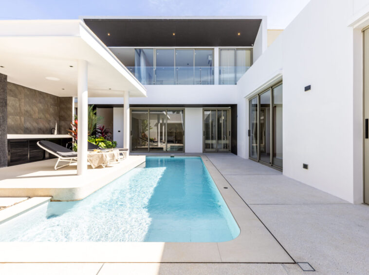 Modern white villa courtyard with a rectangular pool, lounge chairs, and glass doors.** (option 1)