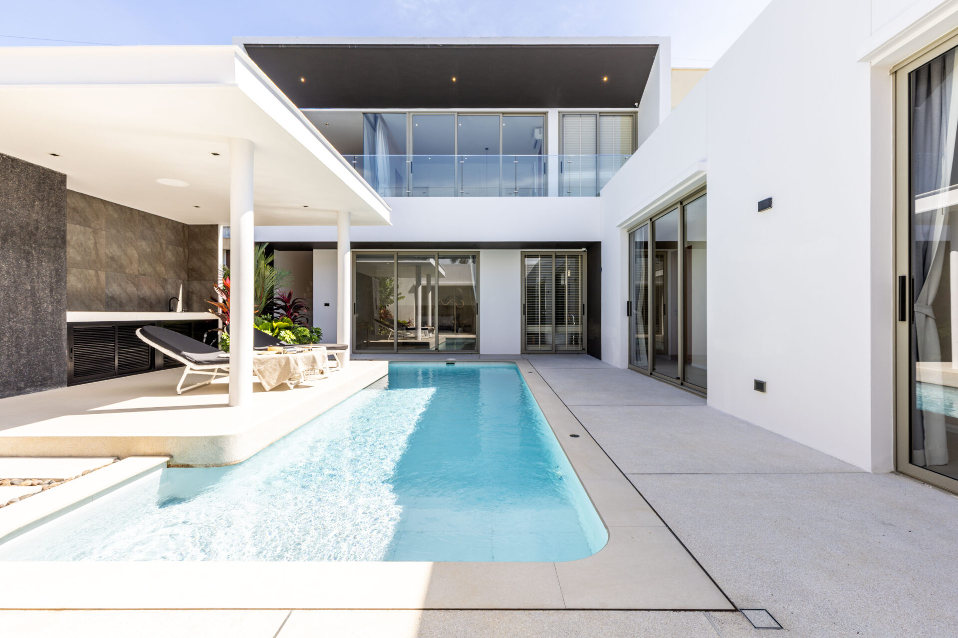 Modern white villa courtyard with a rectangular pool, lounge chairs, and glass doors.** (option 1)