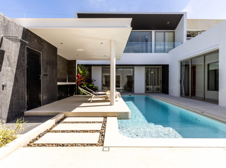 Modern backyard of a contemporary home featuring a rectangular pool, white patio, and lounge chairs.
