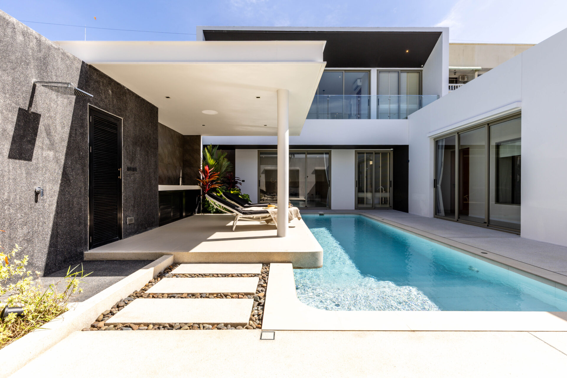 Modern backyard of a contemporary home featuring a rectangular pool, white patio, and lounge chairs.