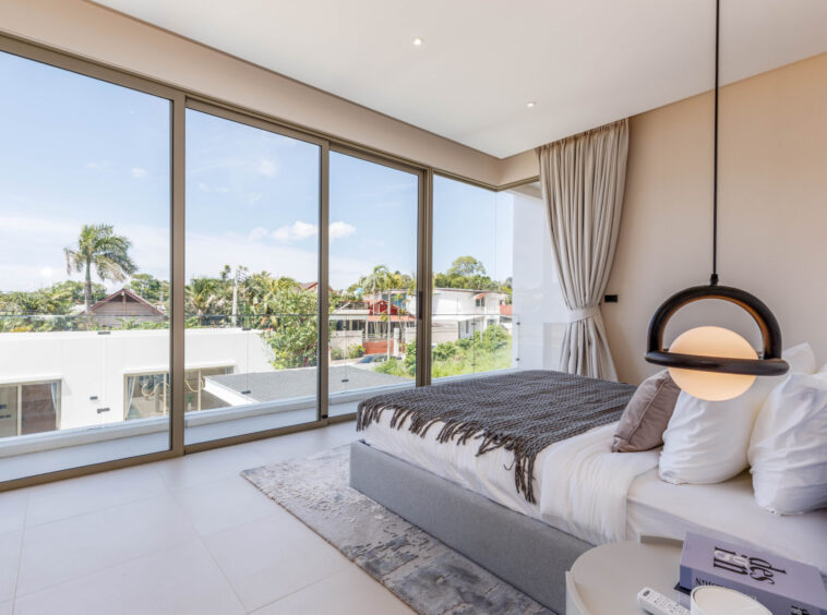 Bright modern bedroom with large glass walls and a round pendant light by the bed.