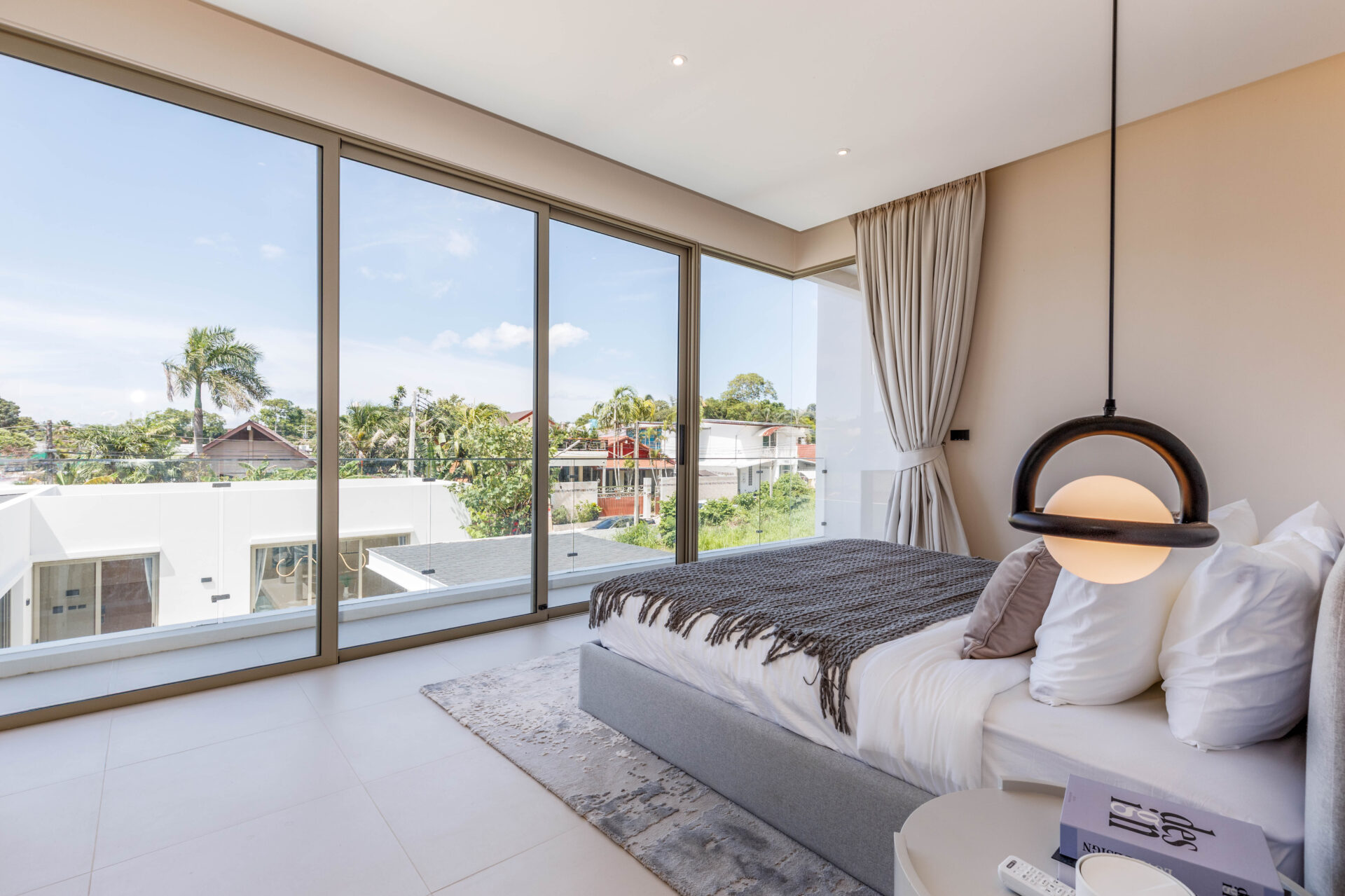 Bright modern bedroom with large glass walls and a round pendant light by the bed.