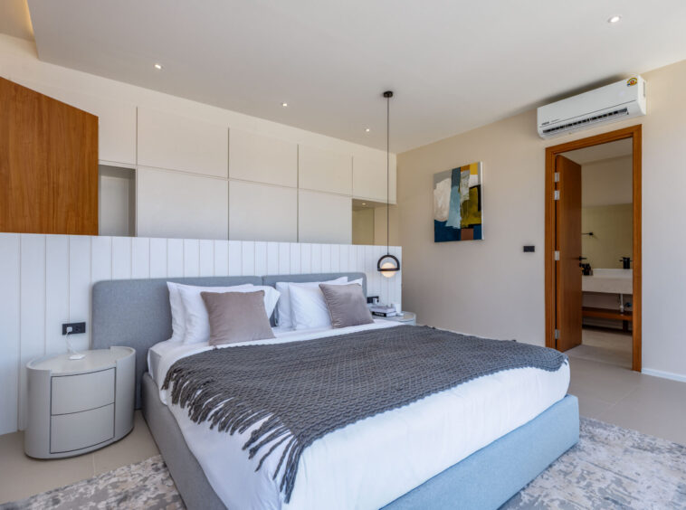 Modern hotel bedroom with a gray upholstered bed, white linens, and a textured gray throw.