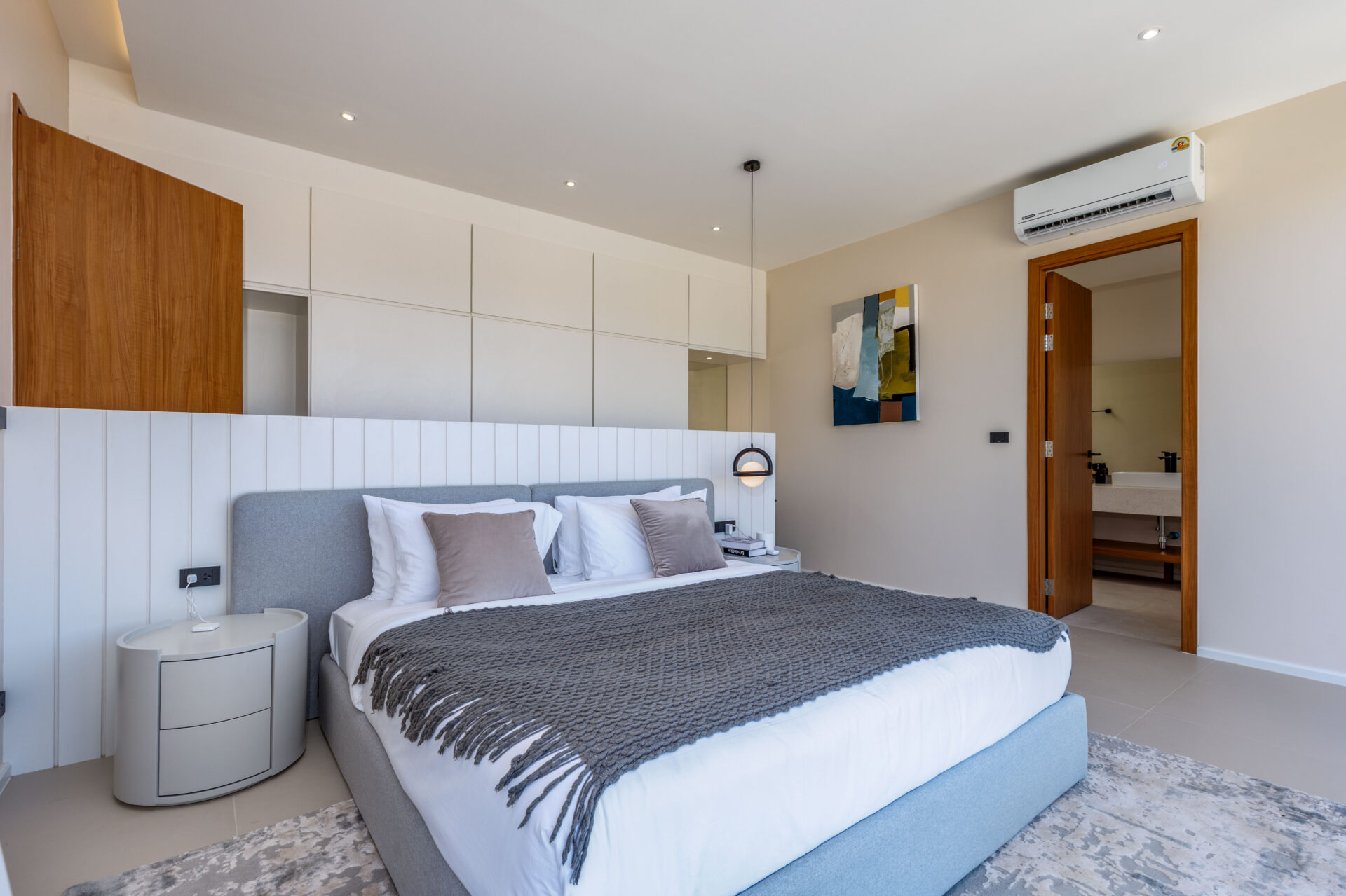 Modern hotel bedroom with a gray upholstered bed, white linens, and a textured gray throw.